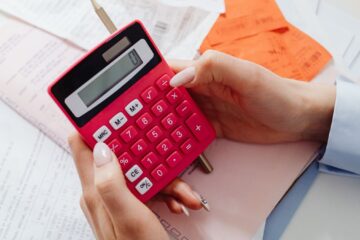 Close-up of hands holding a red calculator, managing finances with documents and receipts.