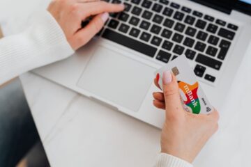 Close-up of a person using a laptop and holding a credit card for online shopping.