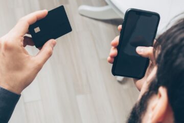 Close-up of man holding a smartphone and credit card, making an online payment indoors.