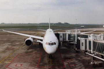 A modern jet airplane docked at an airport terminal gate, ready for boarding on a cloudy day.