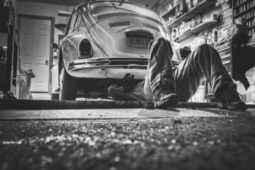Mechanic working beneath a classic Volkswagen Beetle in a vintage garage setting.