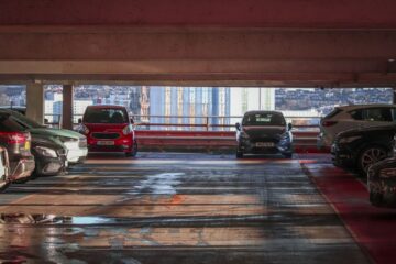 Parked cars in a multi-level parking garage overlooking a cityscape.