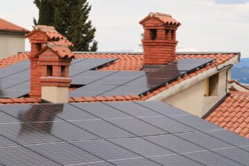 Solar panels on tiled roofs of houses with chimneys, capturing clean energy.