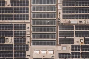 A high-angle drone shot capturing a grid of solar panels on a large industrial rooftop, showcasing renewable energy.