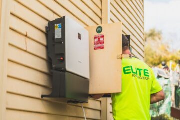 Electrician from Elite Power Group installing a solar inverter outside.